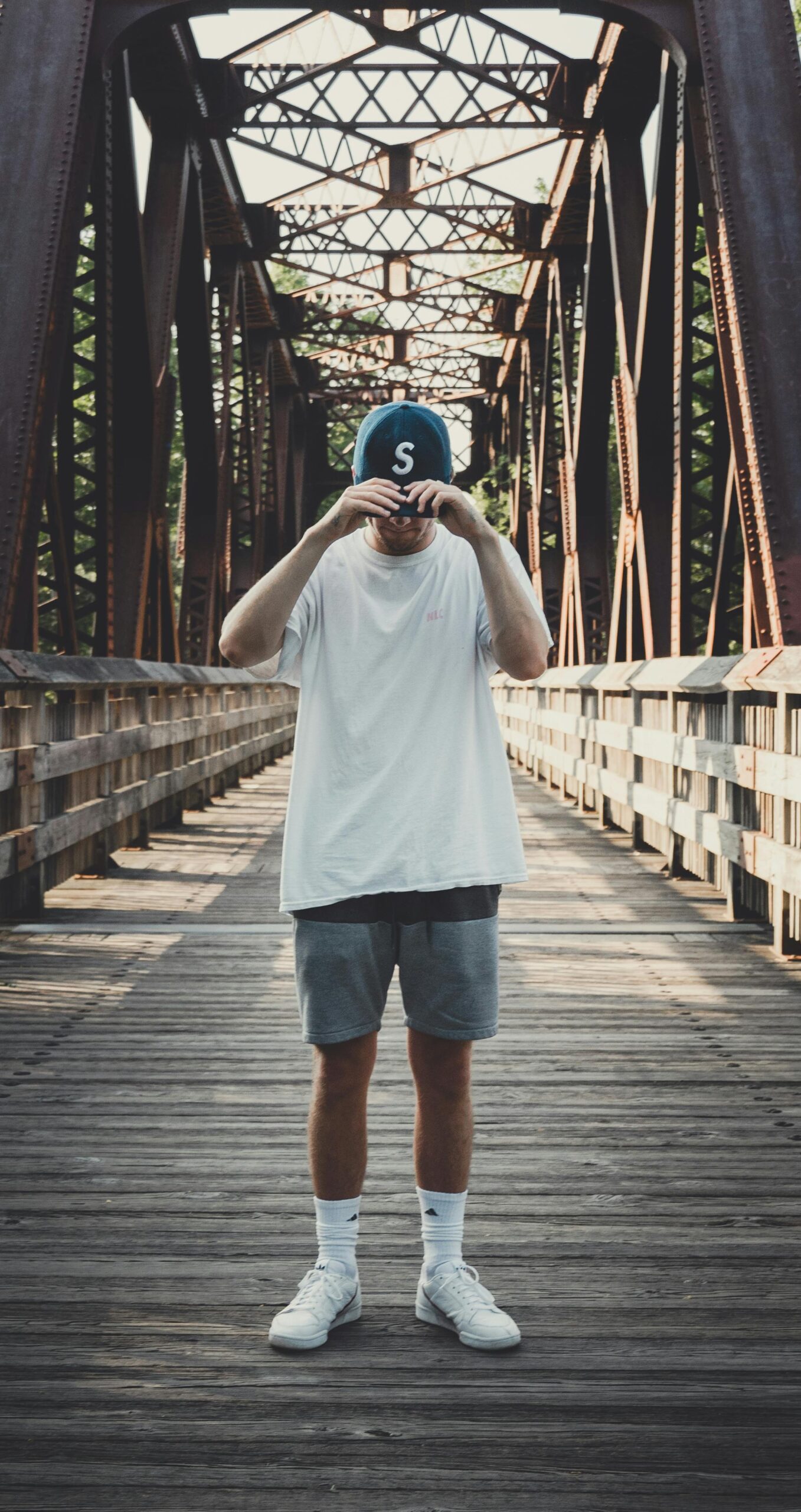 Casual fashion photo of a man posing on a metal bridge on a sunny day.